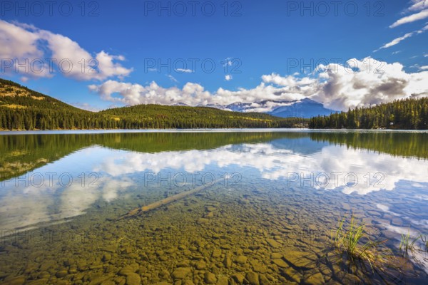 Clear water Pyramid Lake reflects the clouds and pine forests on shore. Frosty morning in the Rocky Mountains, Canada, North America