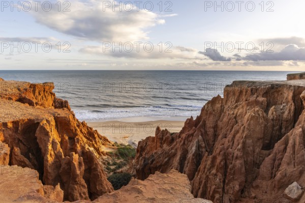 View from one, eroded cliffs of red sand and pebbles with stunning formations illuminated by a warm sunset. Wide beach on the Atlantic Ocean in a landscape shot. Praia da Falésia, Algarve, Portugal, Europe