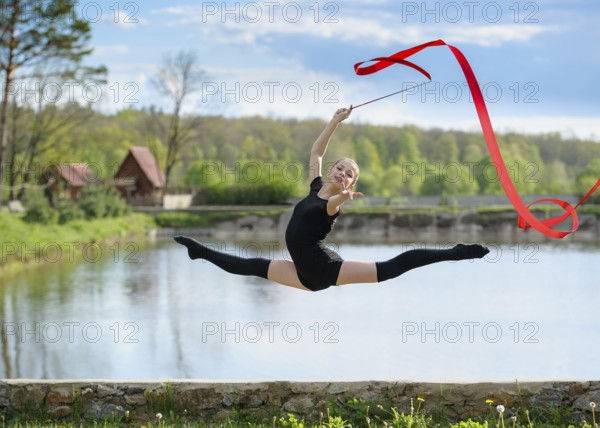 Young rhythmic gymnast doing split jump during ribbon exercises