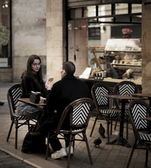 A young couple enjoy some baked goods on an outdoor patio in central Bordeaux, France, Europe
