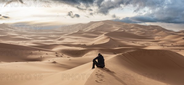 A person sitting in the Erg Chebbi desert in the African Sahara, Morocco, Africa