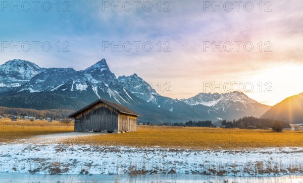 Winter alpine landscape with an aged wooden barn, the Alps mountains, a frozen river at sundown. Picture captured in Austria