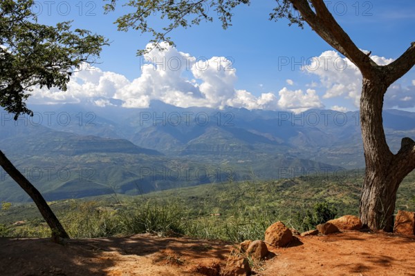 Panoramic view from Barichara, Colombia over green landscape to mountains with blue sky and white clouds along the mountain ridge, trees and red earth in foreground