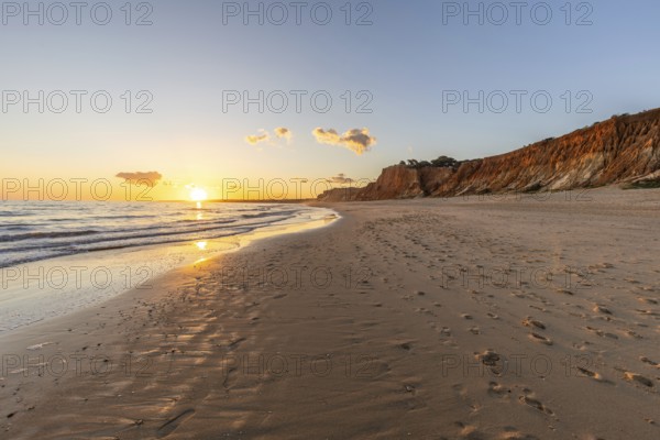 Beautiful sandy beach with red rocks and cliffs. Twilight at sunset with shallow waves on the Atlantic coast in Praia do Poço Velho, Praia da Falésia, Algarve, Portugal, Europe