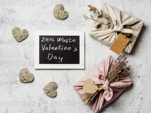 Zero waste Valentine's Day concept. Eco-friendly gift cloth wrapping in Furoshiki style and chalkboard with Zero Waste Valentine's Day letters on gray textured background. Top view or flat lay