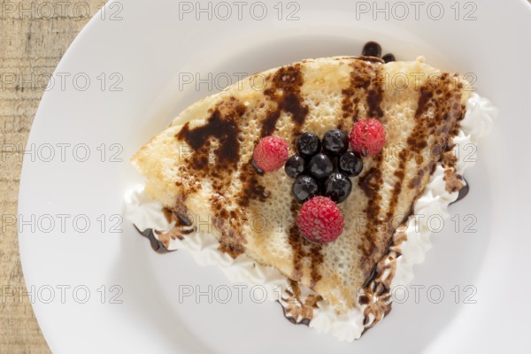 Fresh, golden pancakes with fruit and cream on a white plate with blurred background