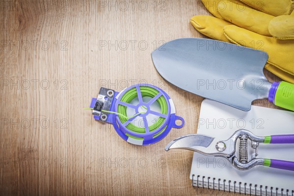 Protective gloves pruning shears garden tie wire hand shovel notepad on wooden board gardening concept