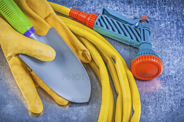 Set of rubber garden hose spray nozzle safety gloves spade on metallic background gardening concept