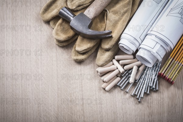 Wooden meter dowels blueprint rolls claw hammer leather protective gloves and metal nails on wood board construction concept