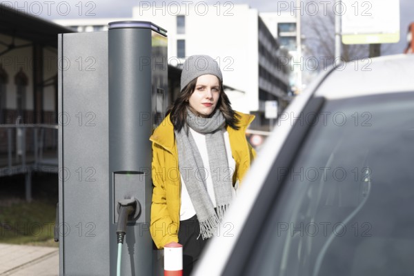 Woman in yellow jacket at e-charging station next to an electric car, environmentally friendly