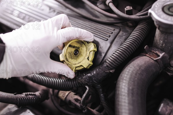 A gloved hand removing the cap from a car engine for maintenance