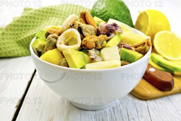 Salad from shrimps, octopus, mussels and calamari with avocado, lettuce, lemon and pineapple in a bowl, green cloth on a background of light wooden boards