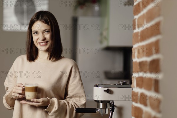 Woman with a cup of coffee beside an espresso machine and brick wall