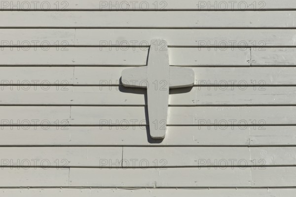 Closeup of white painted wood cross on a white wooden wall