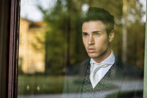Handsome young man or bridegroom looking through the window