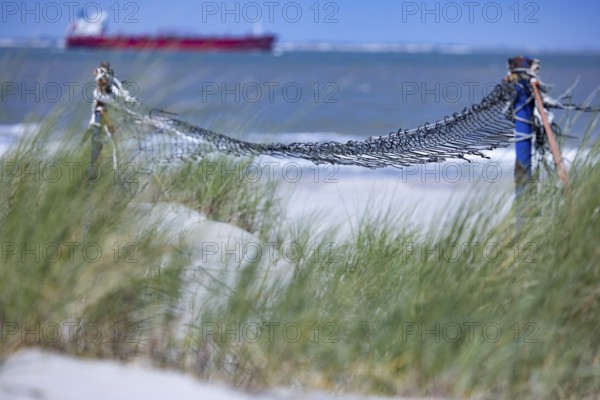 Old, weathered volleyball net in front of grasses on the beach, a ship can be seen in the distance, Groede, Zeeland, Netherlands