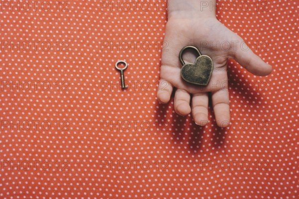 Hand holding a heart shaped lock and key on a red background