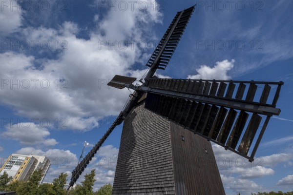 Germany, Berlin, 19.09.2023, Marzahner Bockwindmühle, a trestle windmill in Berlin-Marzahn, the name of the mill type says it all: the mill house stands vertically on a single thick beam, the house tree, which ends just above the ground. The house beam is supported by a four-footed trestle. This allows the mill, which is more than 14 metres high, to be rotated through 360 degrees. Wooden bollards are placed around the mill. They mark the minimum distance so that nobody is hit by the rotating wind blades, which have a span of around 20 metres. 01, Europe
