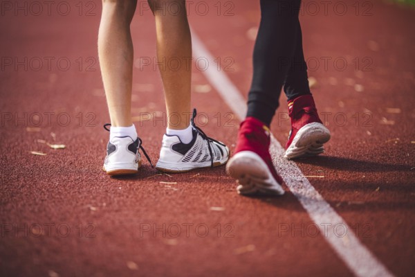 Four legs close-up brother and sister in trainers running on red treadmill in running stadium rear view. Two runners children next to each other on the track. Sport, physical development in school children