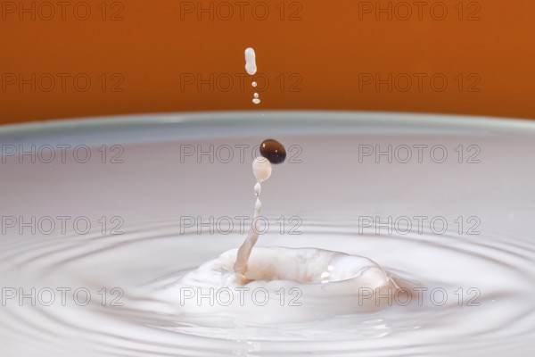 A drop with a splash in an orange environment creates dynamic fluid movement, water droplets, collision, high-speed photography, concept