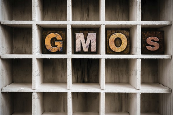 The word GMOS written in vintage ink stained wooden letterpress type in a partitioned printer's drawer