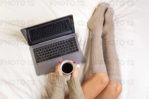 Soft photo of woman on the bed with laptop and cup of coffee in hands, top view point