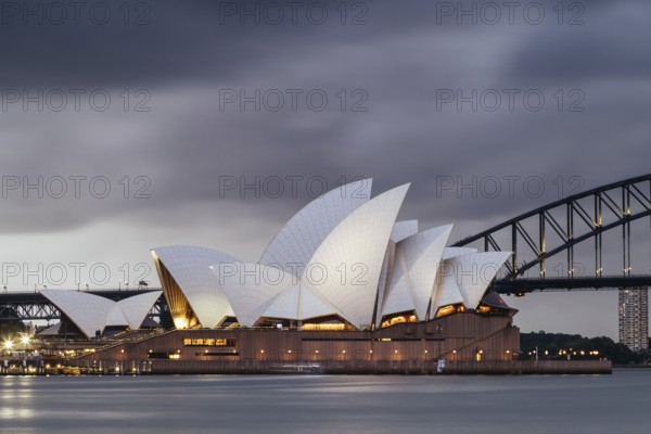 SYDNEY, AUSTRALIA, DECEMBER 03 2023: Sydney Opera House and Harbour Bridge at dusk during a summer storm from Mrs Macquarie's Chair in Sydney, New South Wales, Australia, Oceania