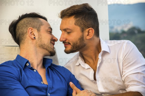 Two gays sitting on chairs at balcony holding hands and looking at each other