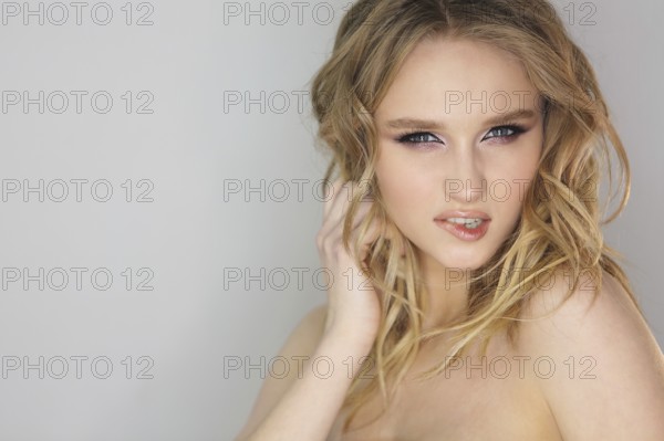 Portrait of the young beautiful woman with blonde curly hair on grey background