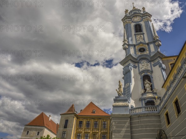 A baroque church tower rising into a cloudy sky, flanked by red-roofed buildings, Dürnstein, Wachau, Danube, Austria, Europe
