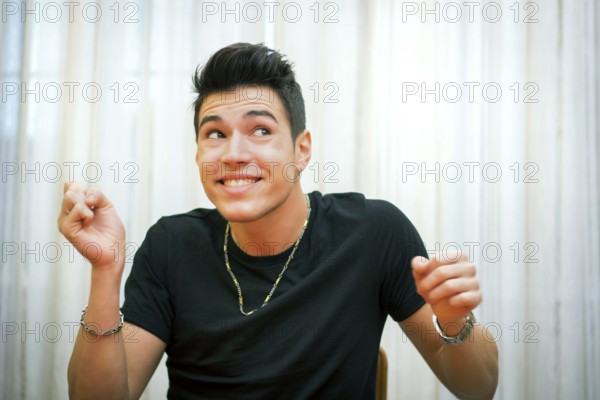Handsome young man pulling a funny face, indoor shot in front of light white curtains