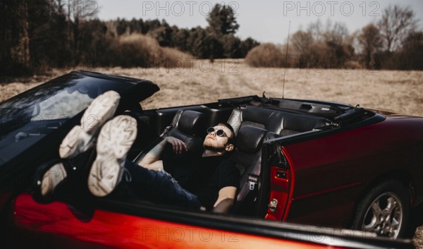 Person relaxing in a red convertible in a peaceful countryside setting