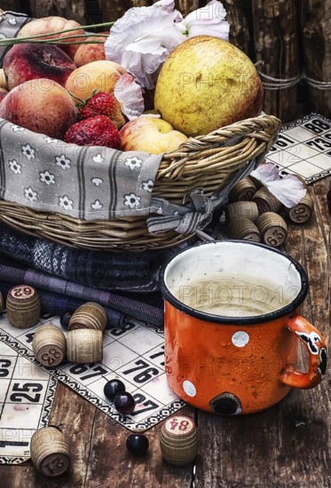 Composition of the enamel cup with water on the background fruit basket and Lotto games for picnic.Photo tinted