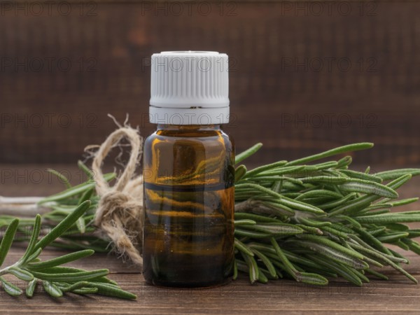 Rosemary essential oil in dark glass bottle and fresh rosemary on dark wooden background with copy space