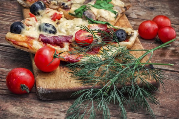 Hunk of delicious meat pizza with bacon and olives on the background of the vegetables.The image is tinted