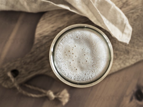Wheat sourdough starter. Top view of glass jar with sourdough starter on wooden cutting board. Copy space for text or design