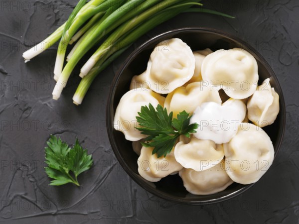 Traditional russian pelmeni, ravioli, dumplings with meat on black concrete background. Top view or flat lay. Russian food and russian kitchen concept