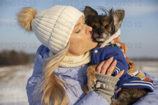 Close-up of a blonde woman hugging her dog. The woman and dog are outside on a winter day. Both are dressed in warm coats