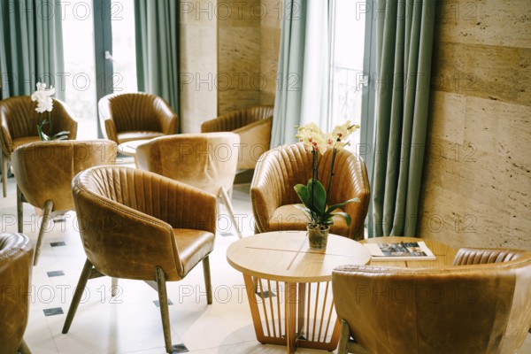 A large hall with exits to the balcony with round tables and flowers and brown armchairs made of genuine leather.