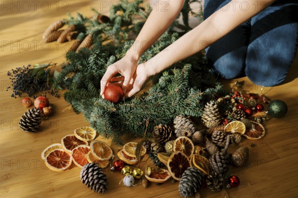 Designer is arranging the Christmas wreath while sitting on the floor. Cropped. Faceless.