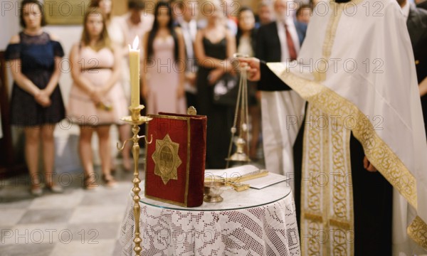 Wedding ceremony in an Orthodox church. The priest in a white cassock stand in the church at the altar, candles and bible near him .