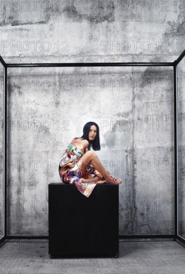 Woman wearing colorful traditional Asian patchwork robe and sitting on a large cube