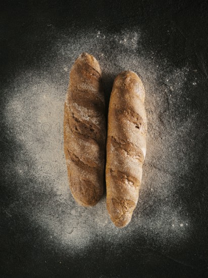 Two whole homemade buckwheat loaf bread with buckwheat flour on black textured background. Top view or flat-lay. Low key