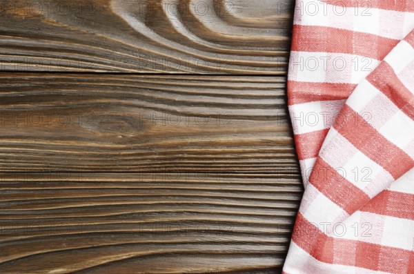 Red checkered napkin on brown wooden kitchen table with copy-space. Top view