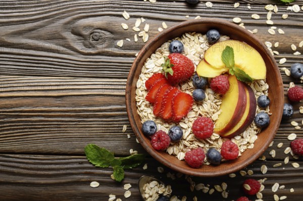 Flat lay of fruit healthy muesli with peaches strawberry almonds and blackberry in clay dish on wooden kitchen table