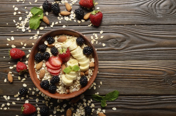 Flat lay top view at Fruit healthy muesli with banana strawberry almonds and blackberry in clay dish on wooden kitchen table