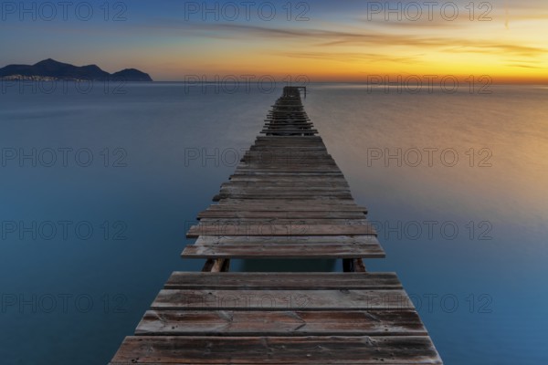 Peaceful sunrise seascape with an old wooden dock leading out into the calm ocean waters of Alcudia Bay