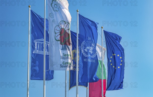 The Flags of European Union, United Nations, Unesco, Bulgaria, and Nessebar city waving in the wind. EU, UN, Unesco, Bulgaria, and Nessebar flags against a blue sky, Europe