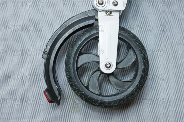 Front wheel and tire of a scooter with a black tire and metal attachment on a grey backdrop