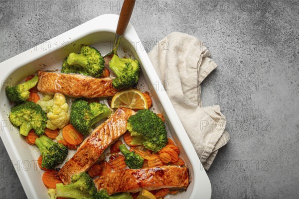Top view of healthy baked fish salmon steaks, broccoli, cauliflower, carrot in casserole dish on gray stone background. Cooking a delicious low carb dinner, healthy nutrition concept. Space for text, food photography